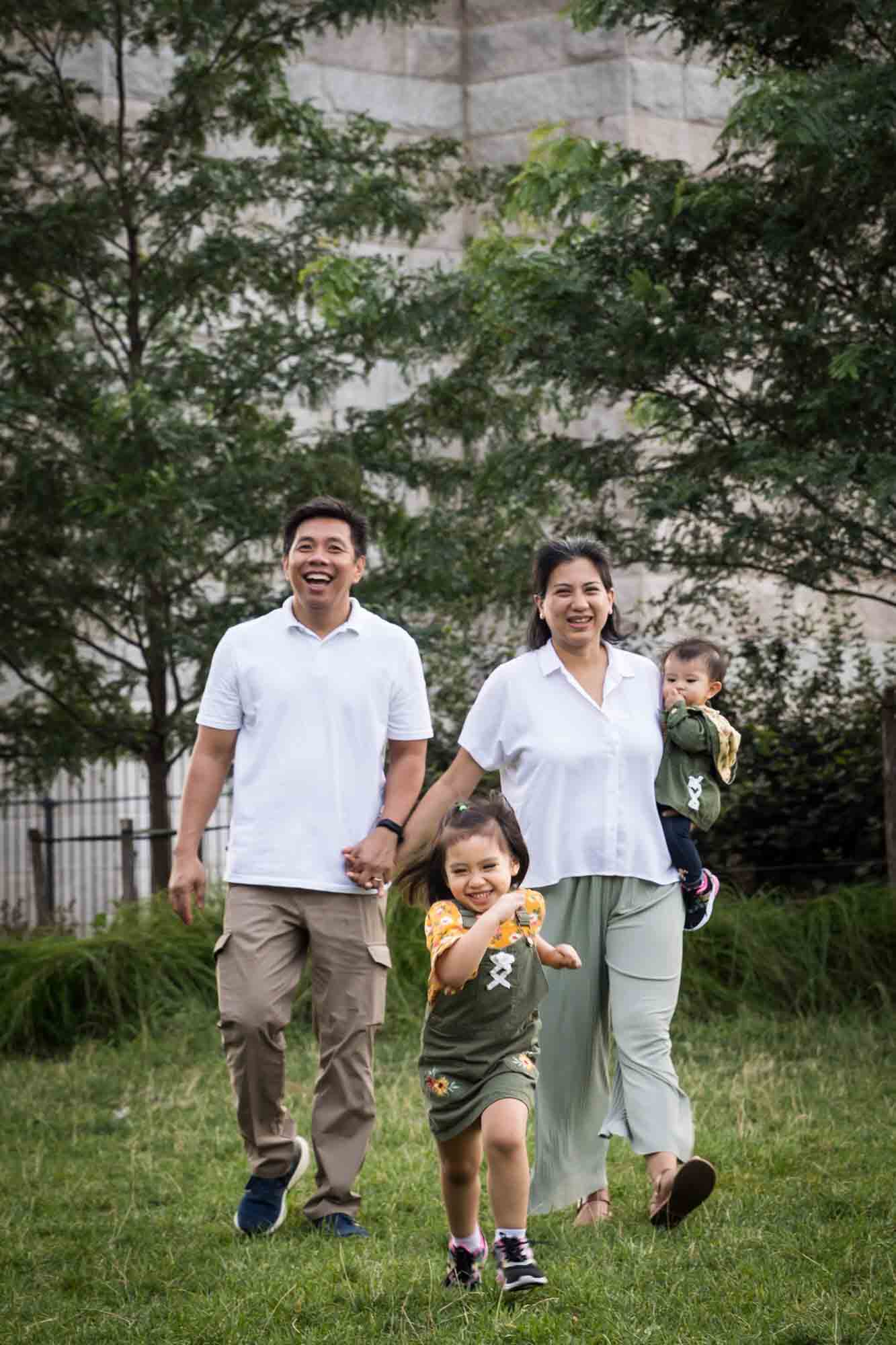 Little girl running in front of parents for an article on Brooklyn Bridge Park family portrait tips for young children