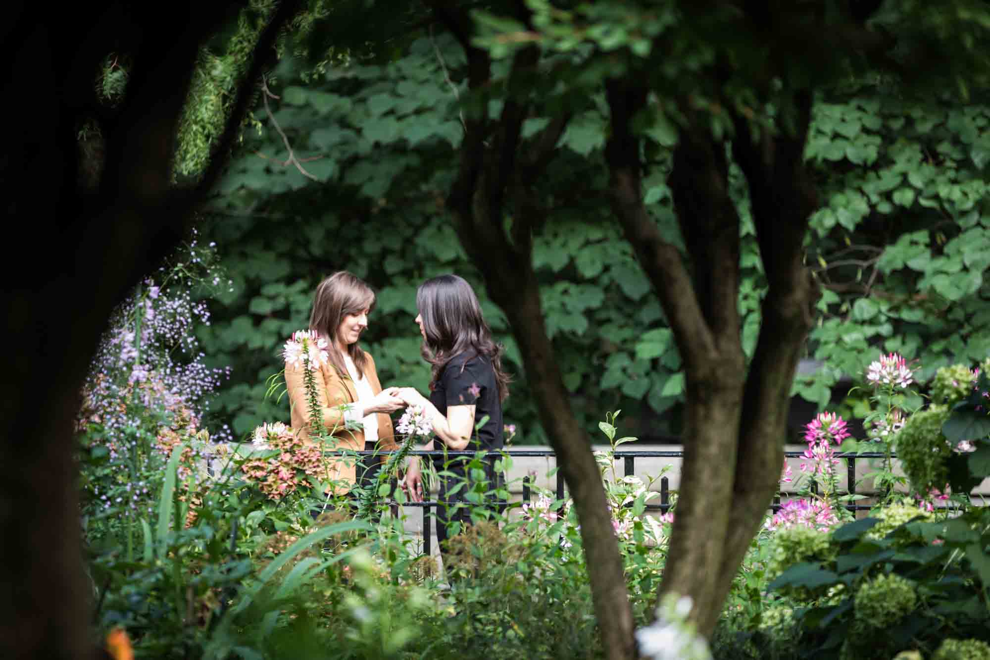 Two women standing in Riverside Park in front of gate and flowers for an article on how to produce a movie-themed surprise proposal