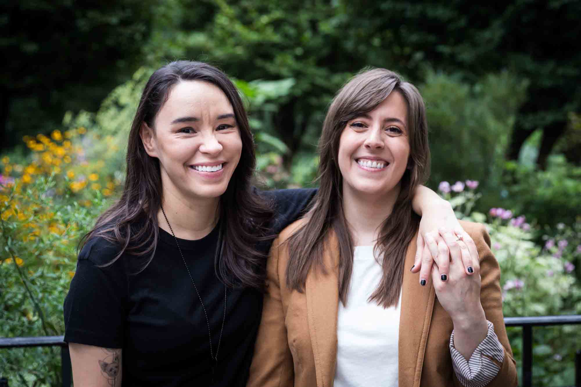 Two women standing in Riverside Park surrounded by green foliage and flowers for an article on how to produce a movie-themed surprise proposal