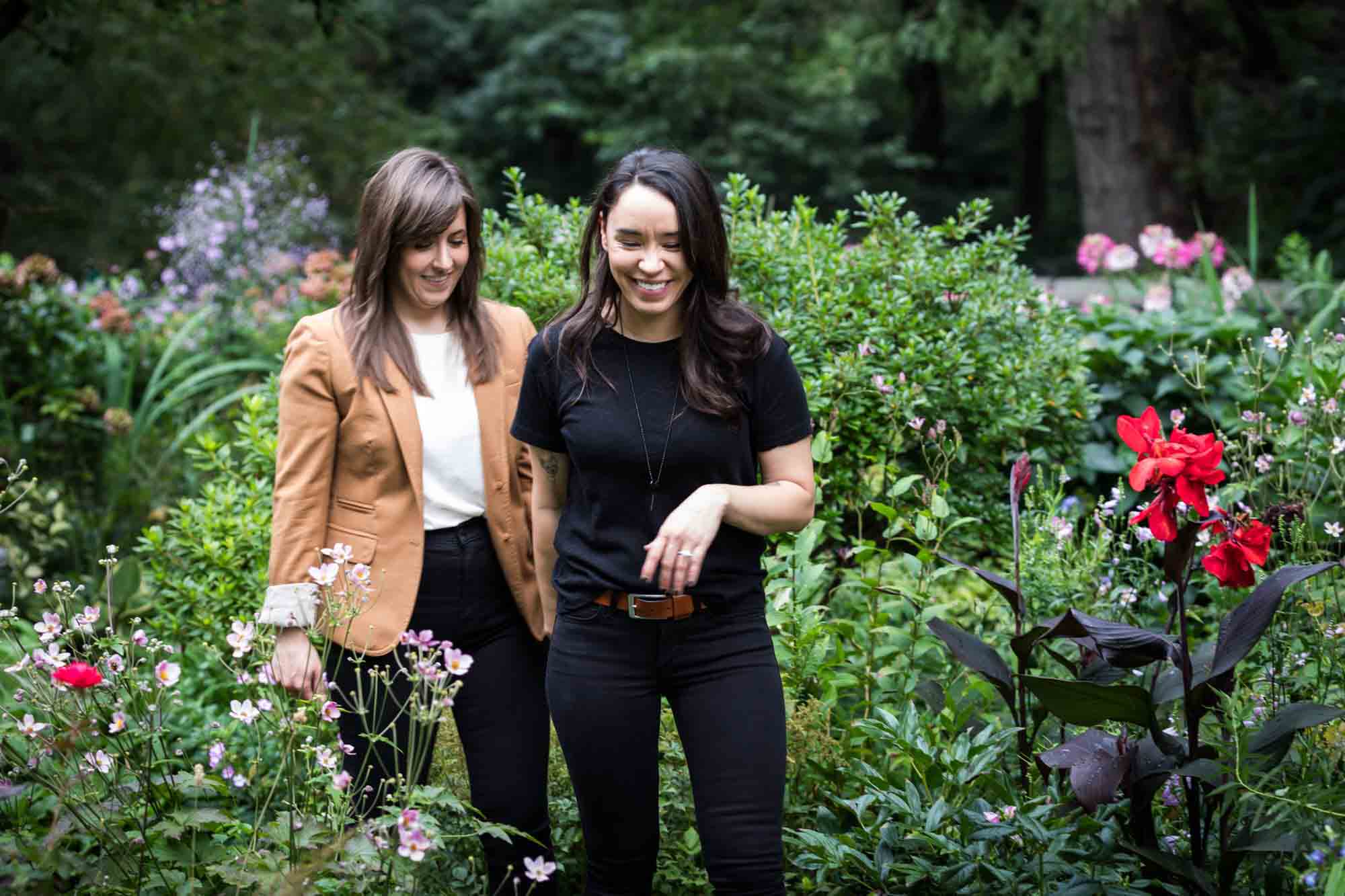 Two women walking through green foliage and flowers for an article on how to produce a movie-themed surprise proposal