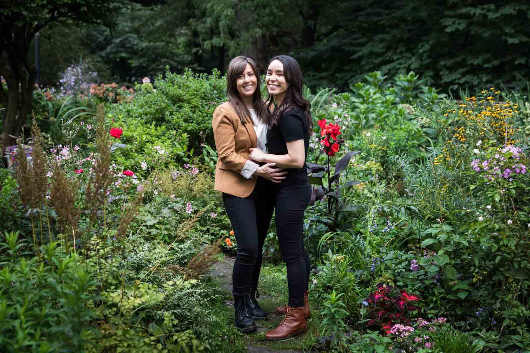 Two women standing in Riverside Park surrounded by green foliage and flowers for an article on how to produce a movie-themed surprise proposal