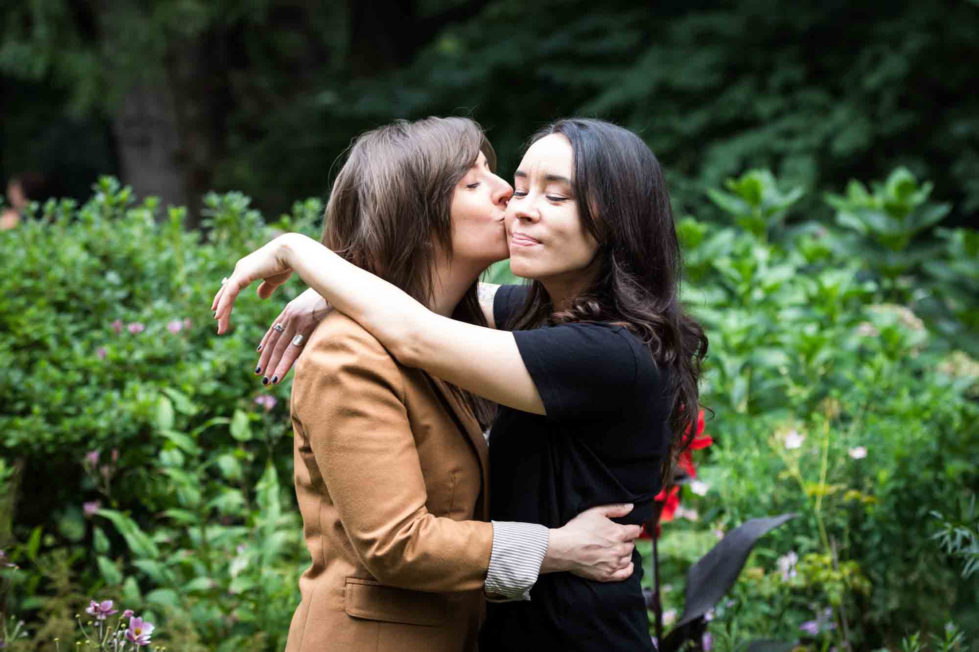 Two women kissing in Riverside Park surrounded by green foliage for an article on how to produce a movie-themed surprise proposal