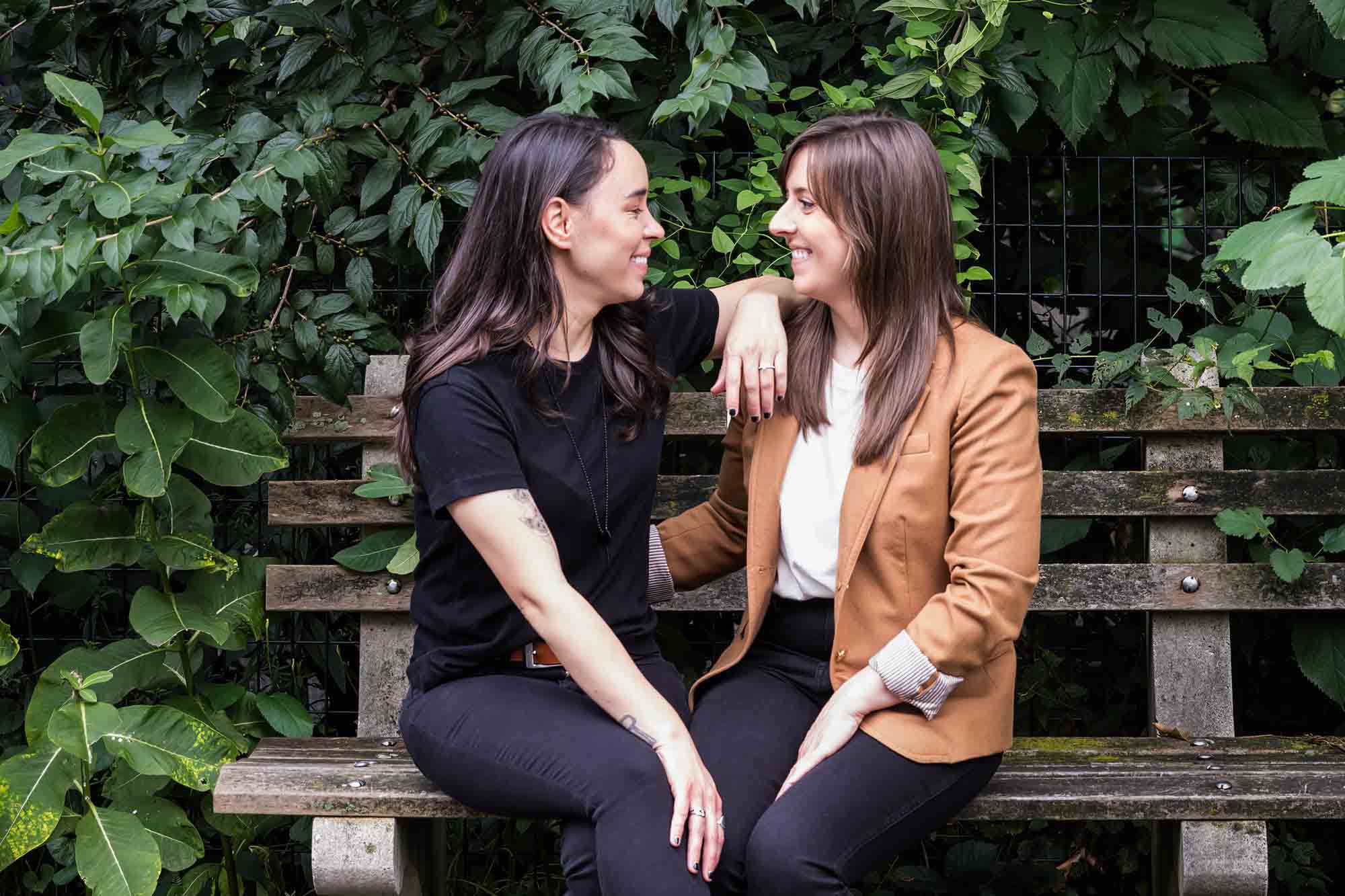 Two women sitting on a bench in front of green foliage in Riverside Park for an article on how to produce a movie-themed surprise proposal