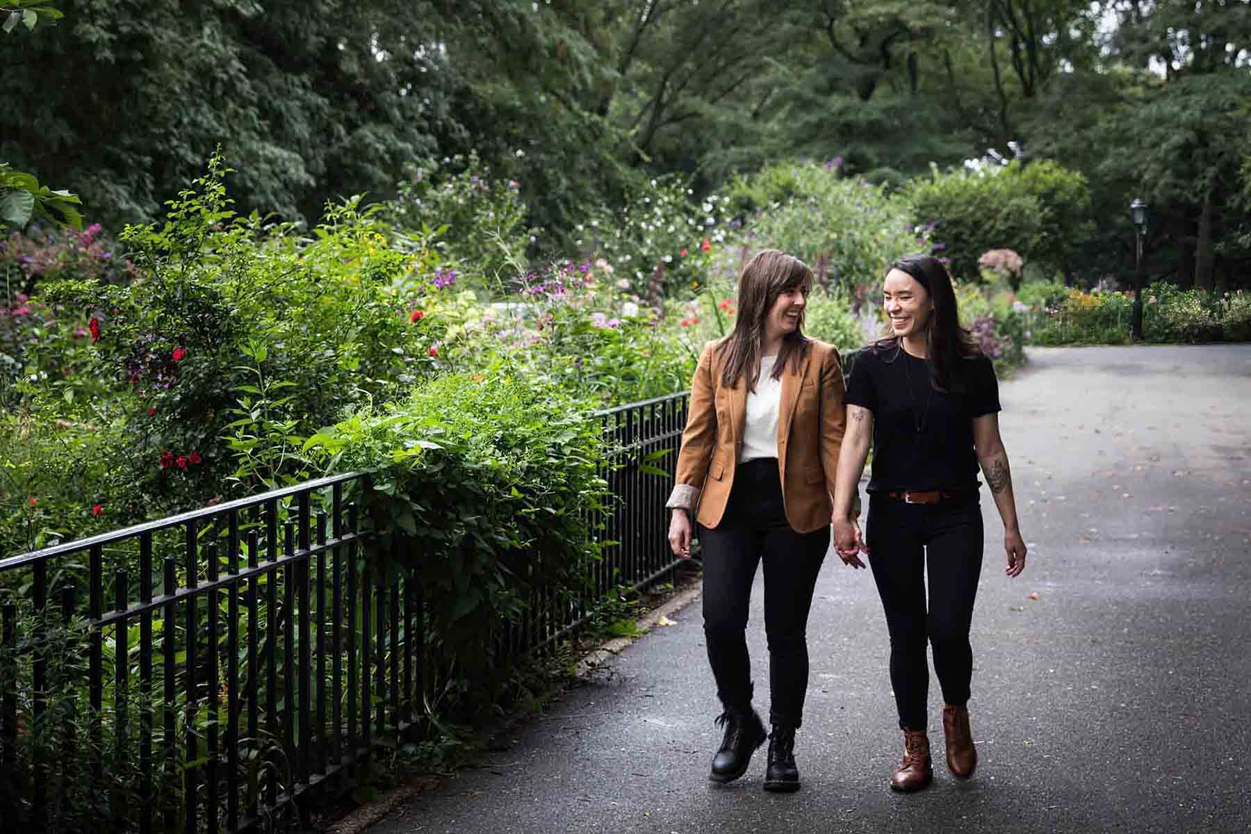 Two women walking hand-in-hand in Riverside Park by a gated garden for an article on how to produce a movie-themed surprise proposal