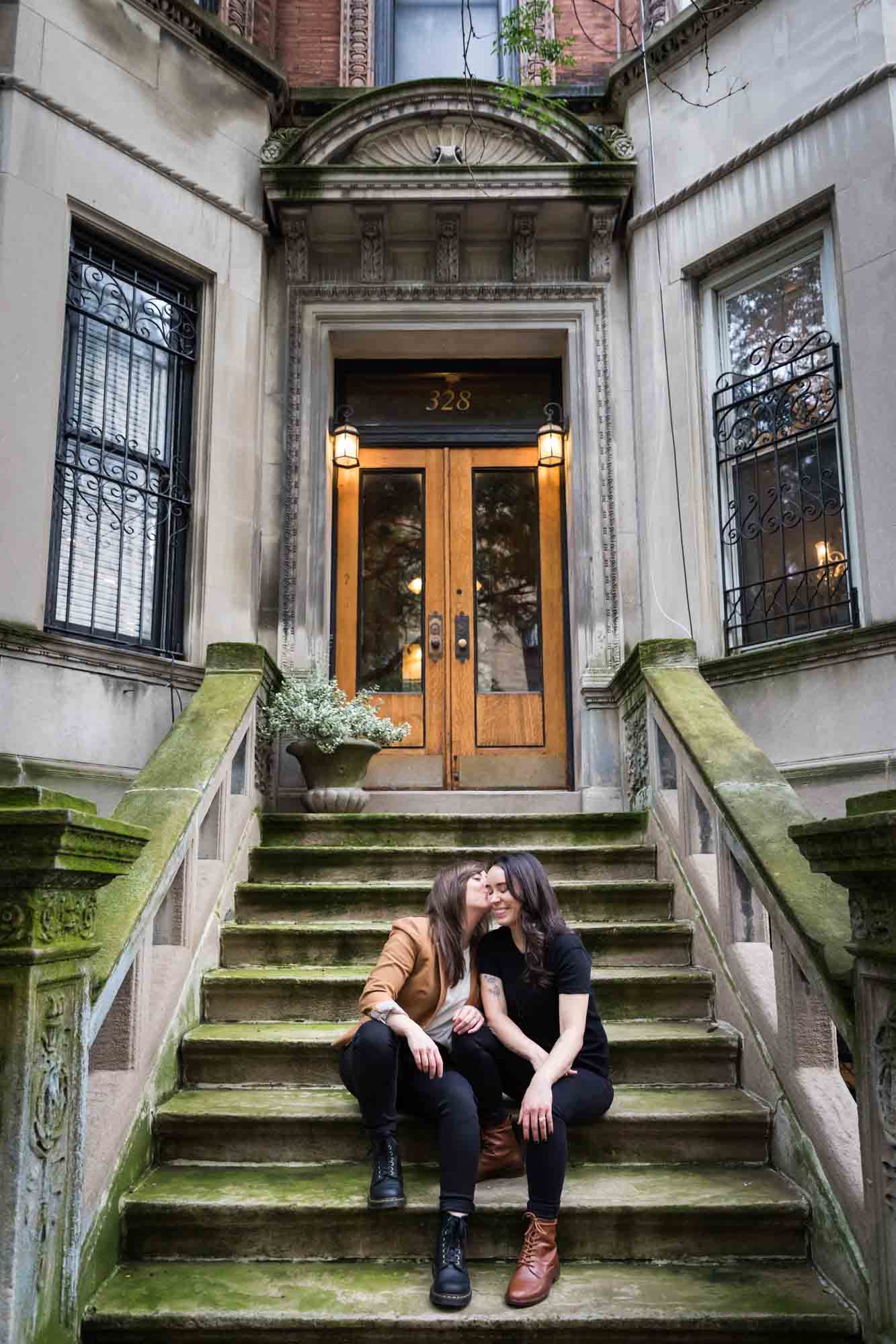 Two women kissing on a stone staircase of a brownstone in NYC for an article on how to produce a movie-themed surprise proposal