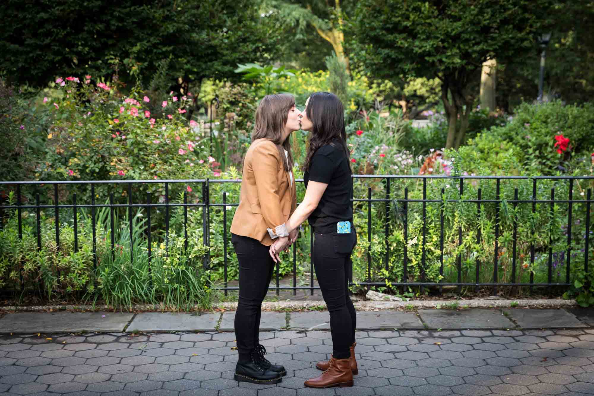 Woman wearing brown jacket kissing another woman during Riverside Park surprise proposal