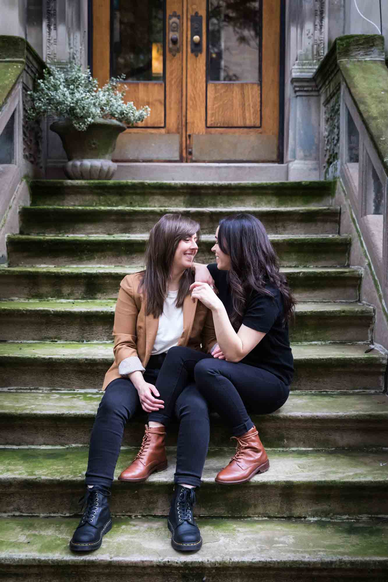 Two women sitting on a stone staircase of a brownstone in NYC for an article on how to produce a movie-themed surprise proposal