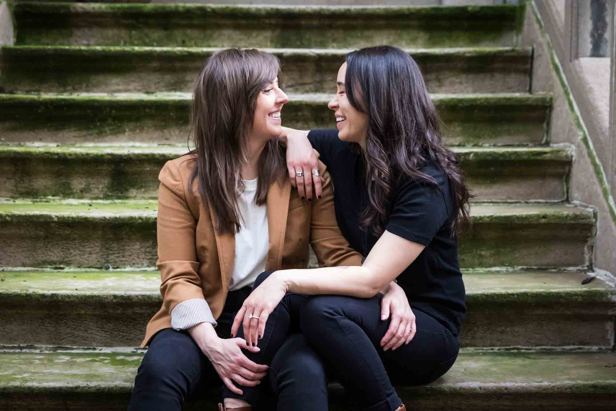 Two women sitting on a stone staircase of a brownstone in NYC for an article on how to produce a movie-themed surprise proposal