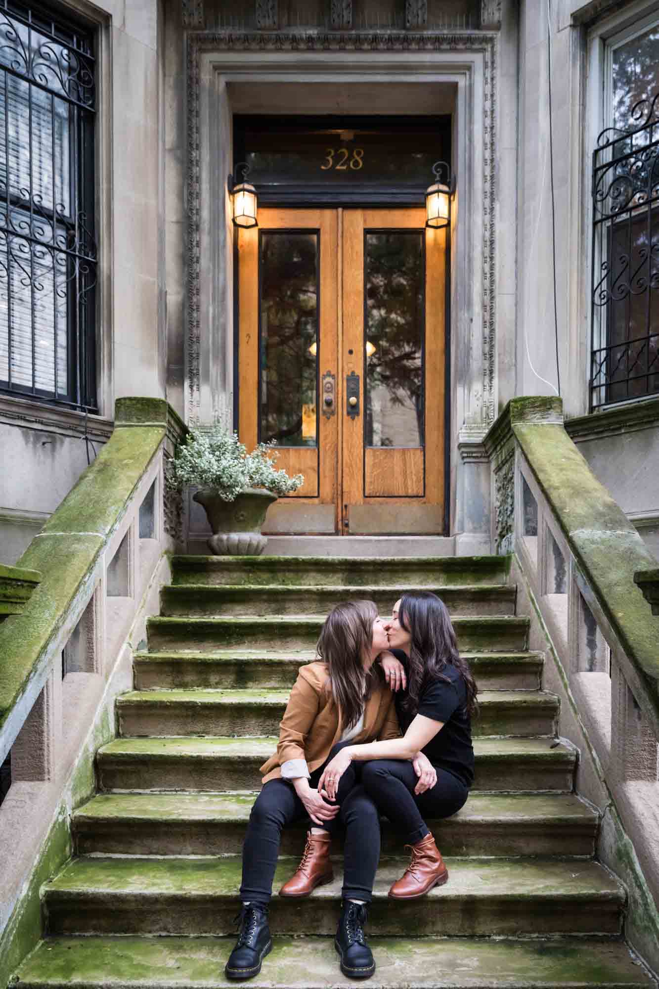 Two women kissing on a stone staircase of a brownstone in NYC for an article on how to produce a movie-themed surprise proposal