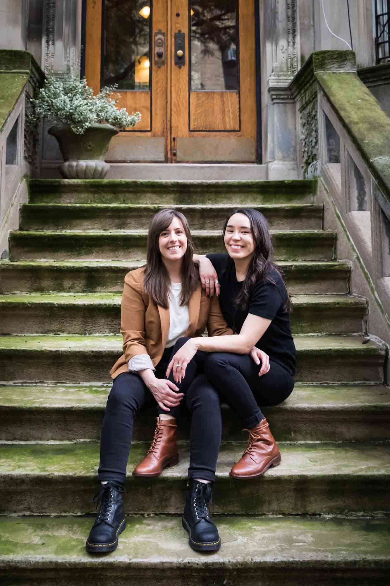 Two women sitting on a stone staircase of a brownstone in NYC for an article on how to produce a movie-themed surprise proposal