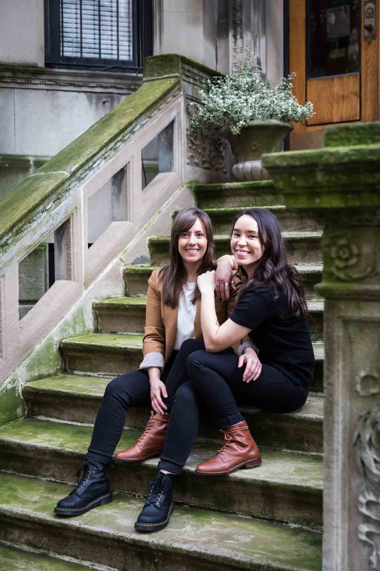 Two women sitting on a stone staircase of a brownstone in NYC for an article on how to produce a movie-themed surprise proposal