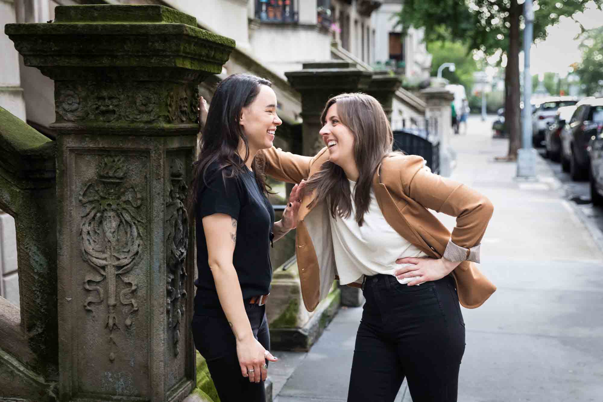 Two women leaning against a stone staircase pillar on a sidewalk in NYC for an article on how to produce a movie-themed surprise proposal