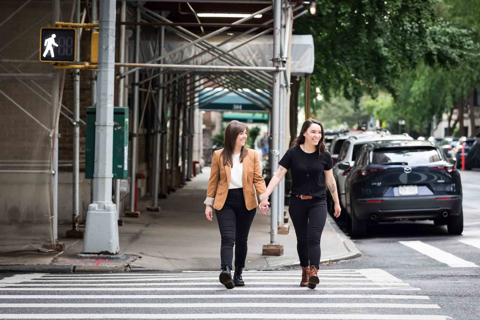 Two women holding hands and walking in a crosswalk in NYC for an article on how to produce a movie-themed surprise proposal