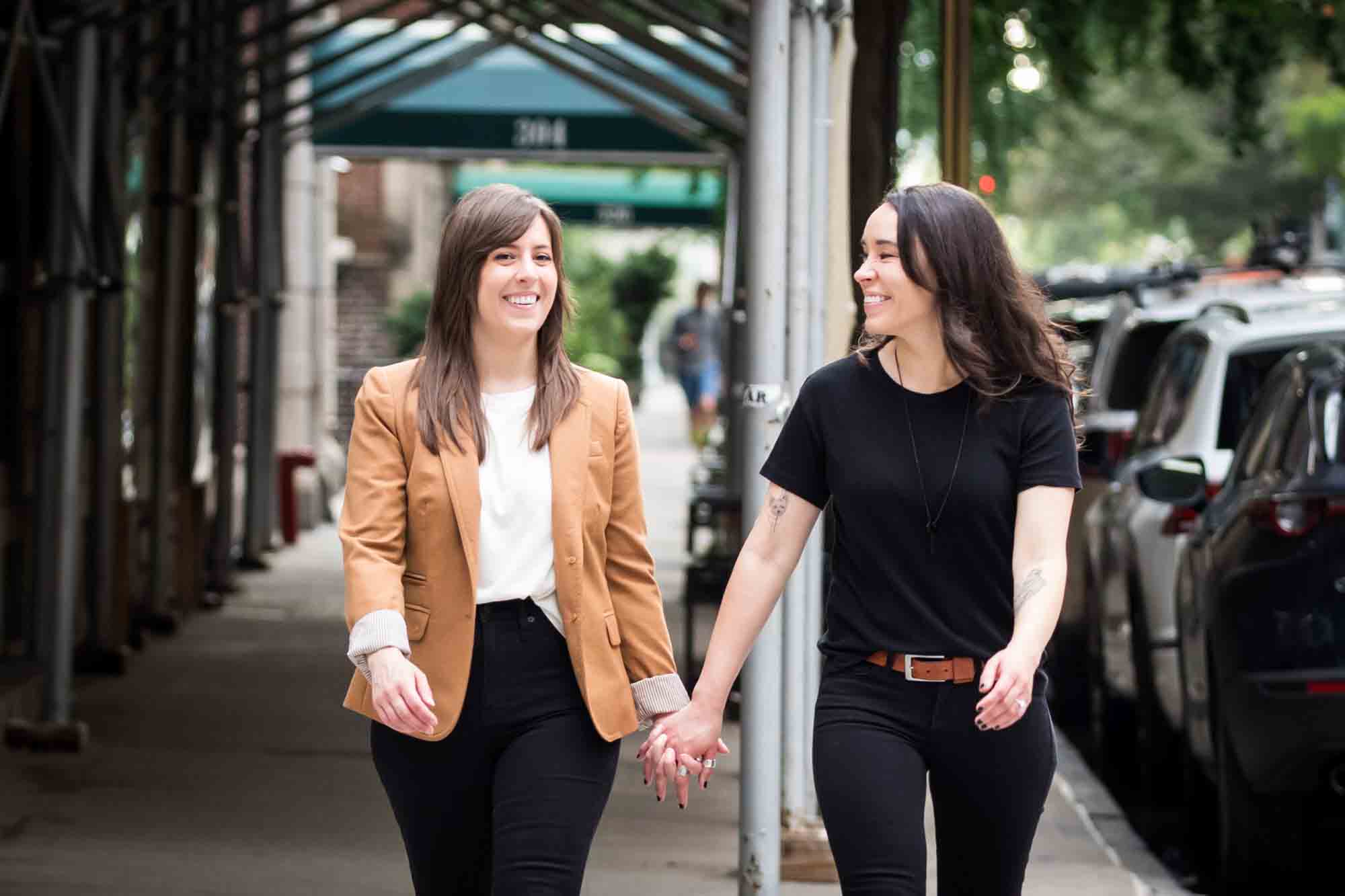 Two women holding hands and walking in a crosswalk in NYC for an article on how to produce a movie-themed surprise proposal