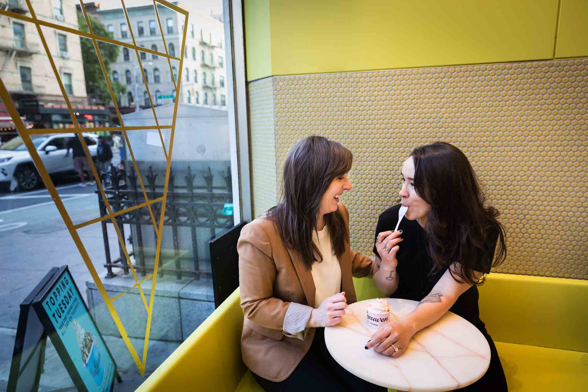 Two women eating ice cream at a table against a yellow wall