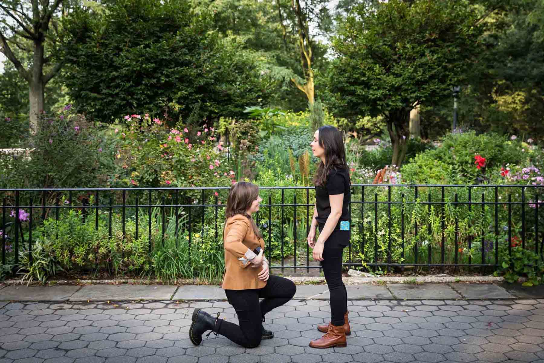Woman on one knee pulling out engagement ring box during Riverside Park surprise proposal