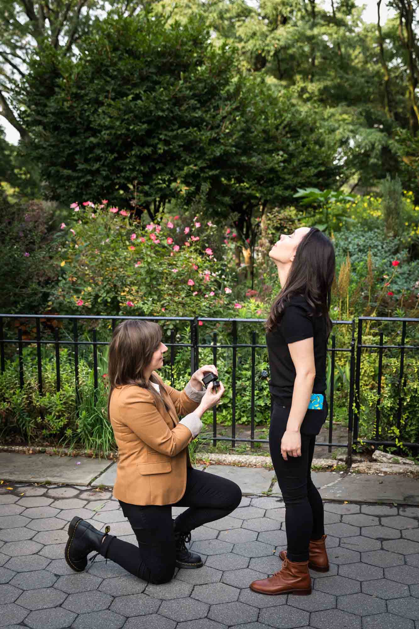 Woman on one knee showing engagement ring to another woman during Riverside Park surprise proposal