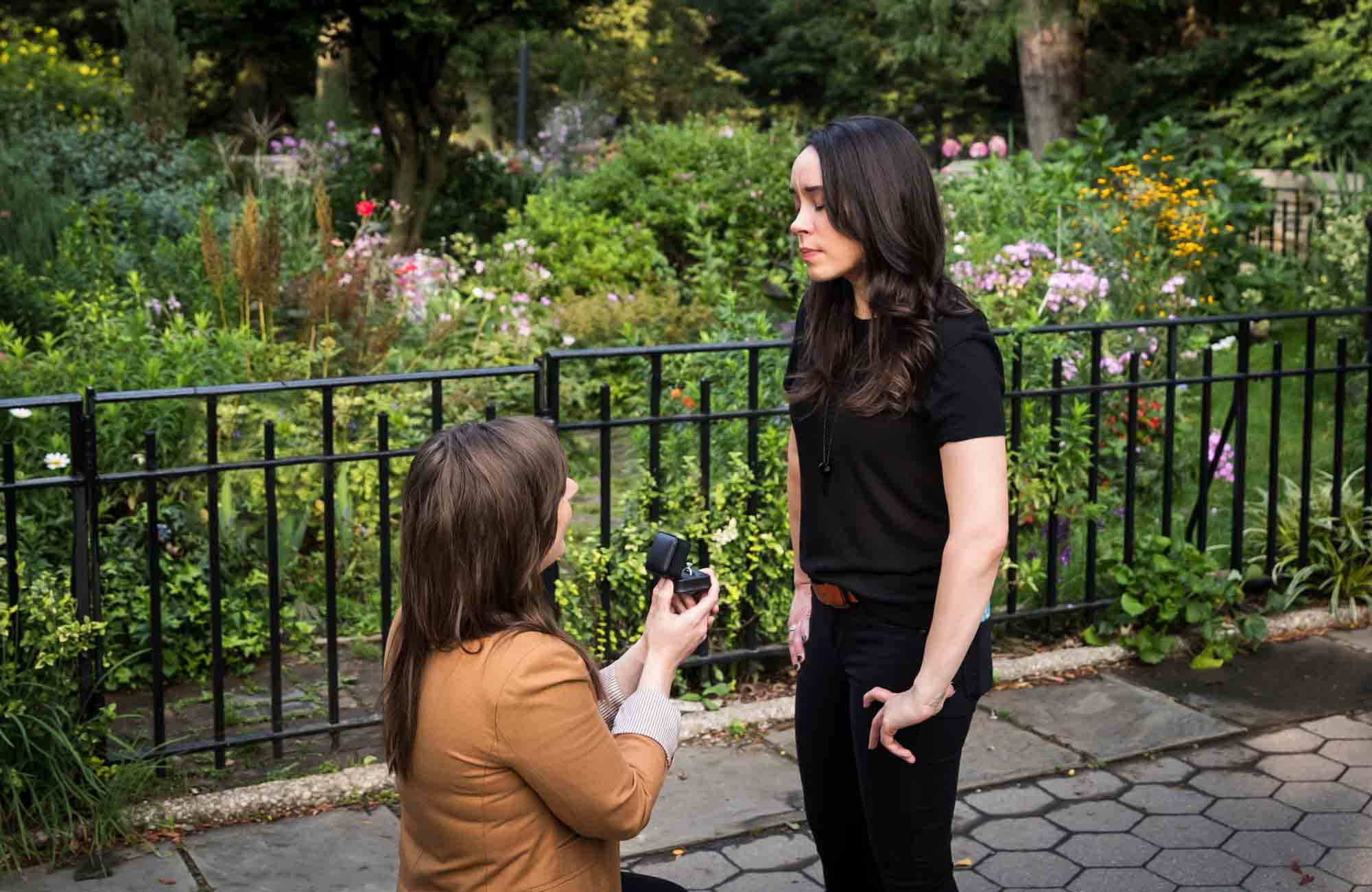 Woman on one knee showing engagement ring to another woman during Riverside Park surprise proposal