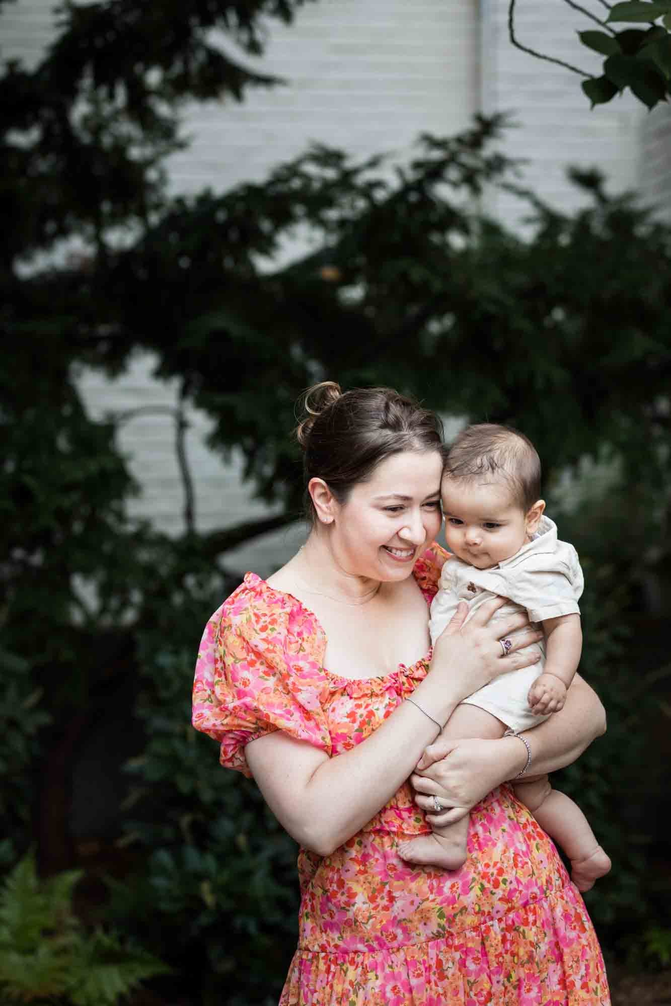 Mother in red floral dress holding baby boy during a Brooklyn Commons family portrait session