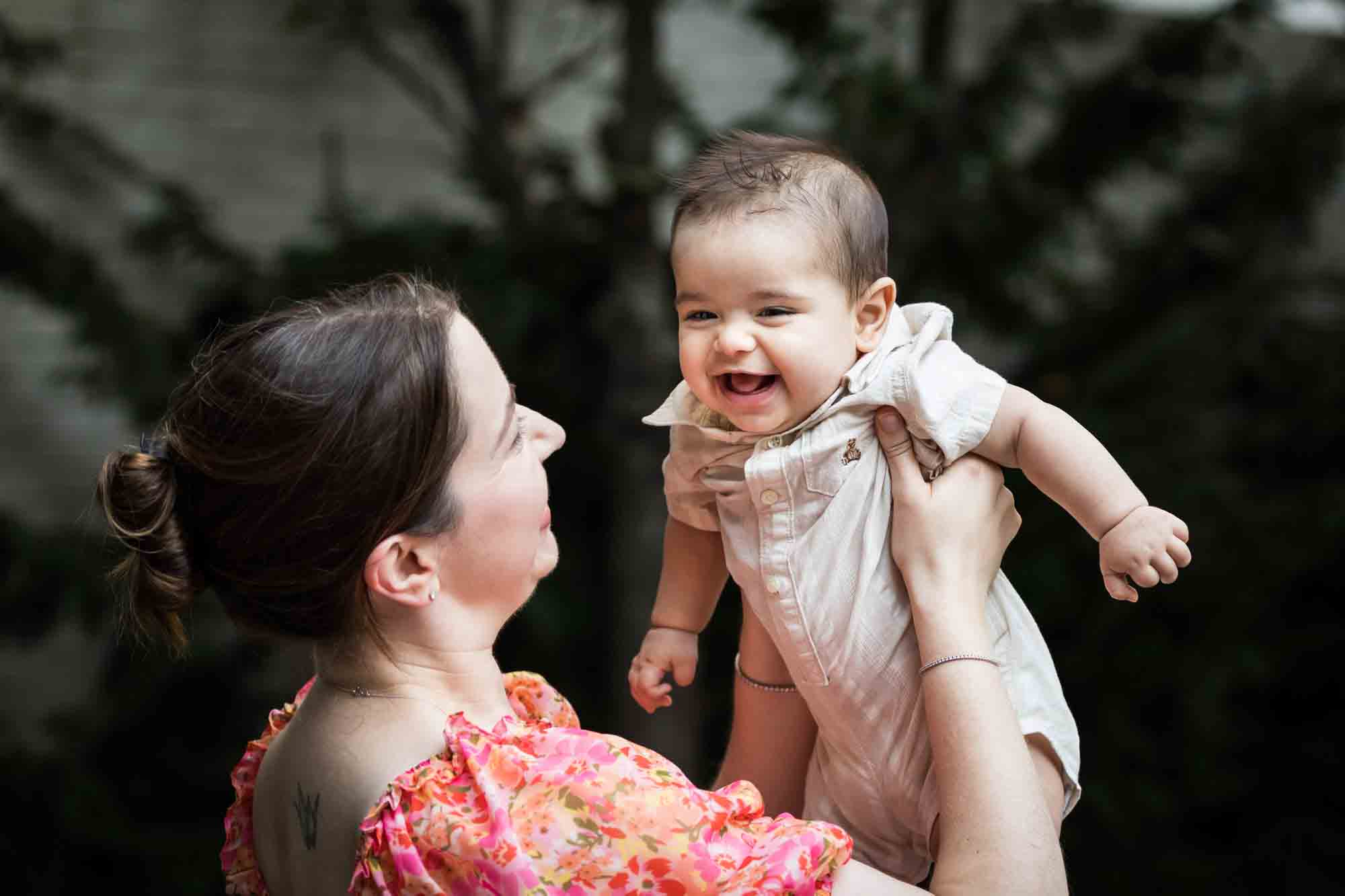 Mother in red floral dress holding baby boy during a Brooklyn Commons family portrait session