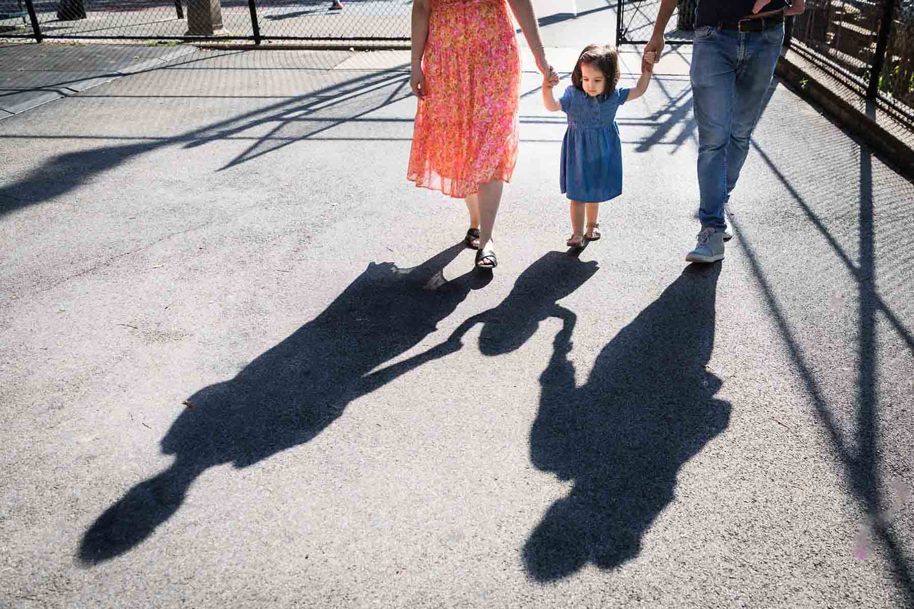 Shadow of little girl in blue dress holding parents's hands on playground