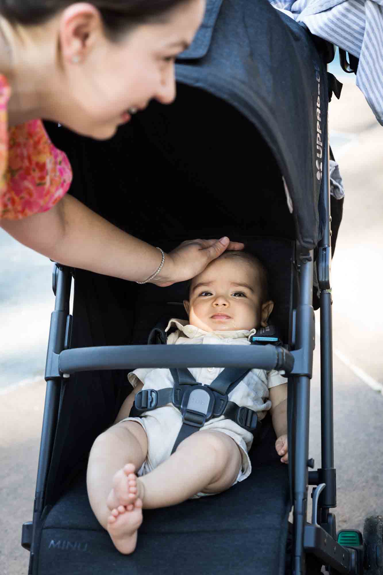 Mother patting baby's head in a stroller during a Brooklyn Commons family portrait session