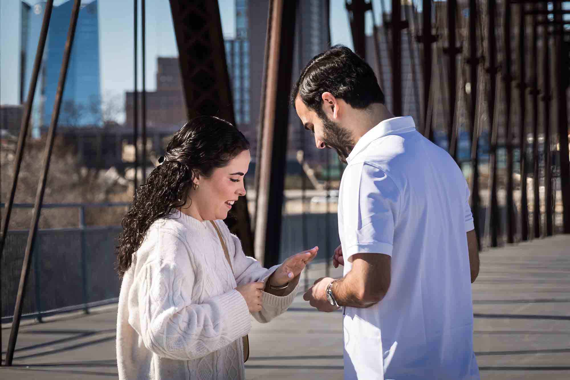 Woman looking at hand with engagement ring in front of man during a Hays Street Bridge proposal