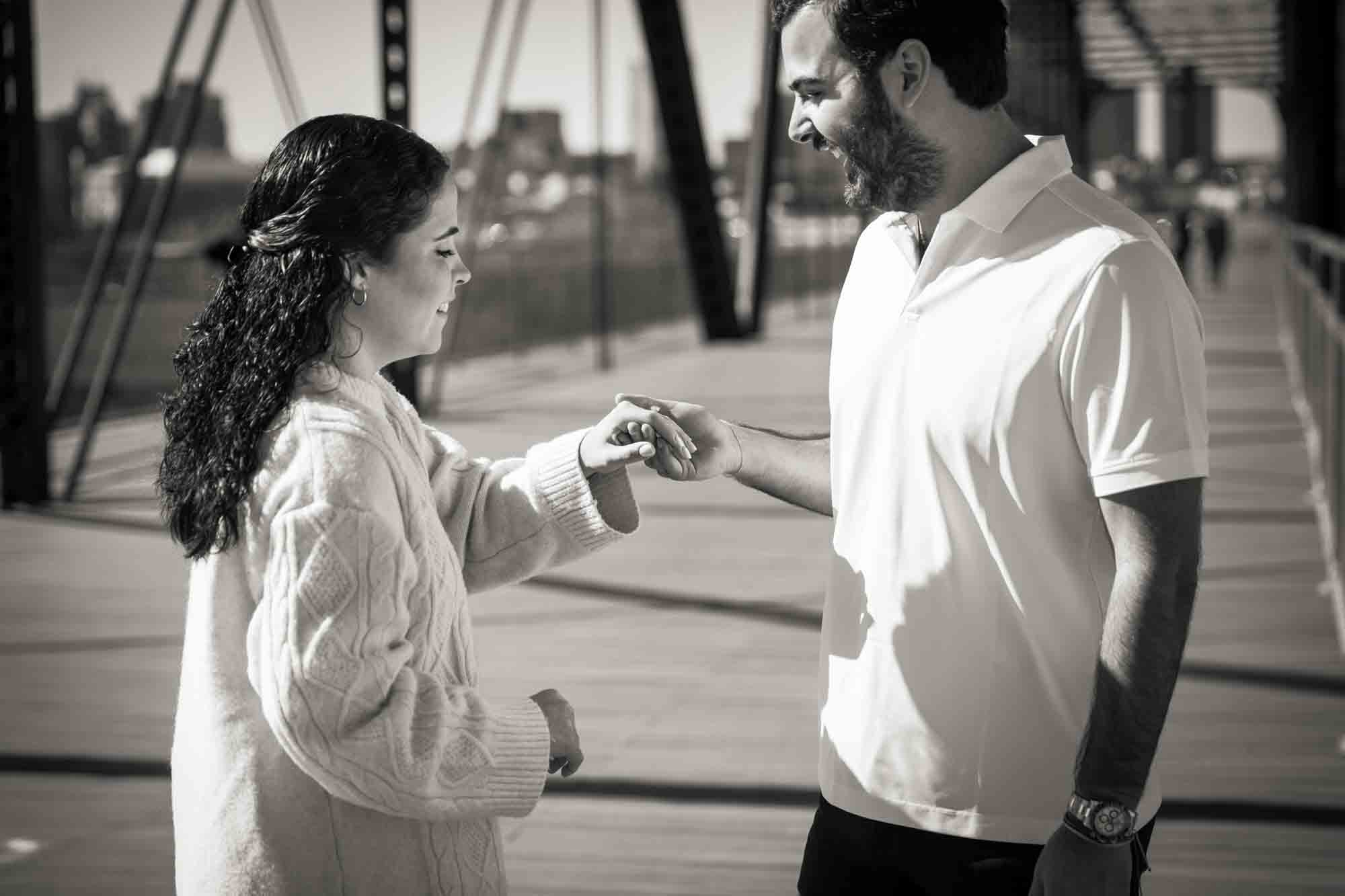 Black and white photo of man holding woman's hand and looking at engagement photo during a Hays Street Bridge proposal