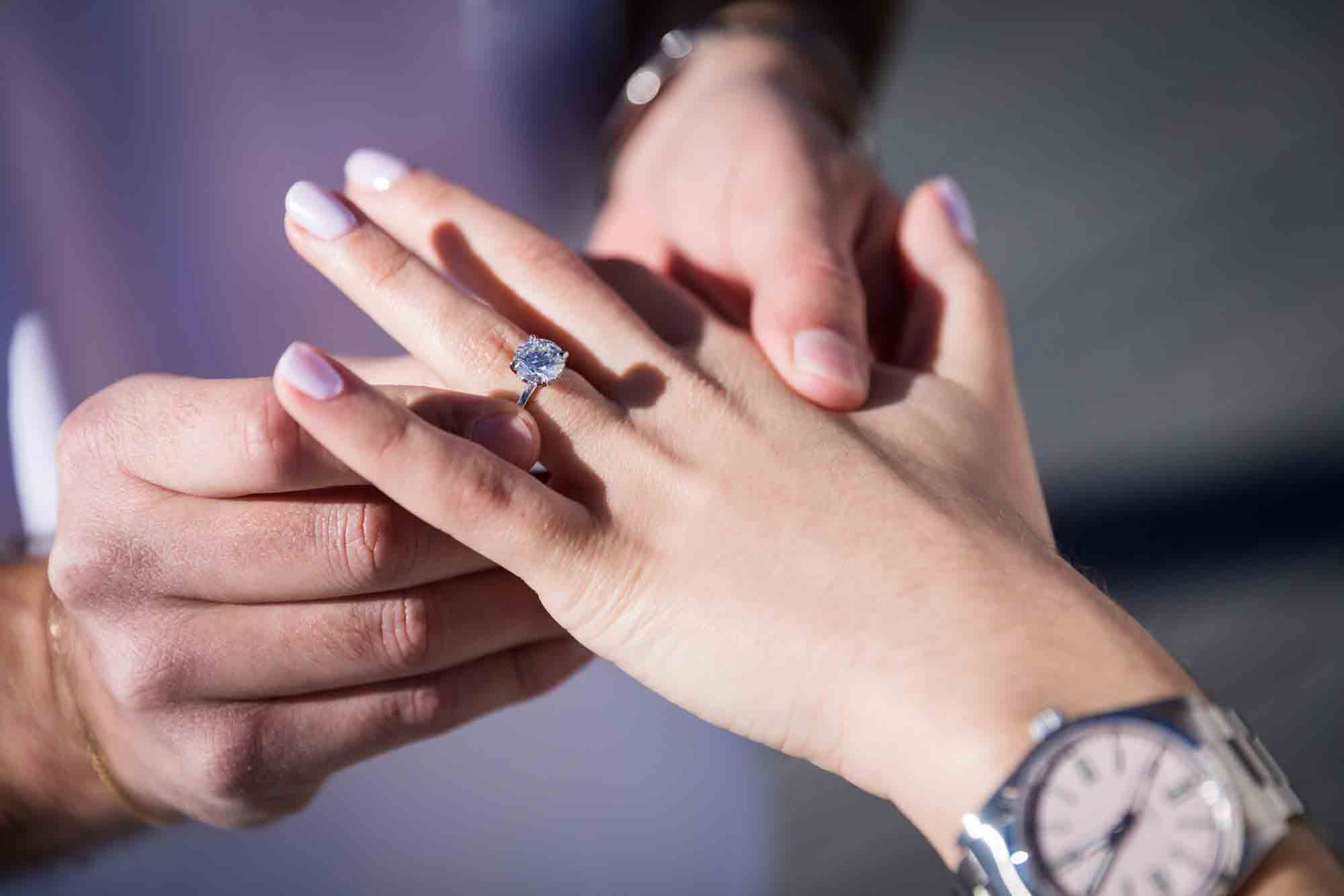 Close up of man putting diamond engagement ring on to woman's finger