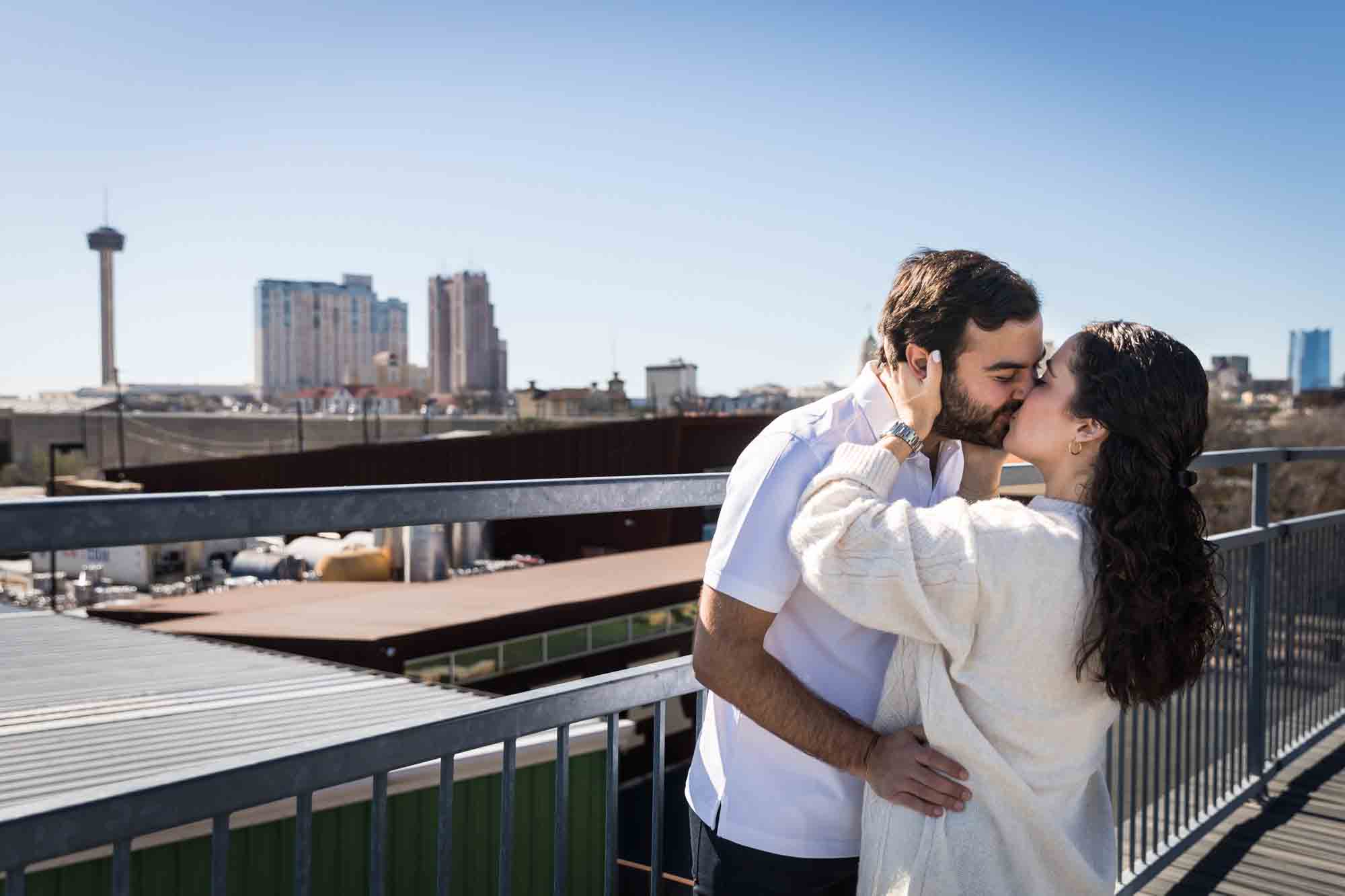 Couple kissing with San Antonio skyline in the background during a Hays Street Bridge proposal