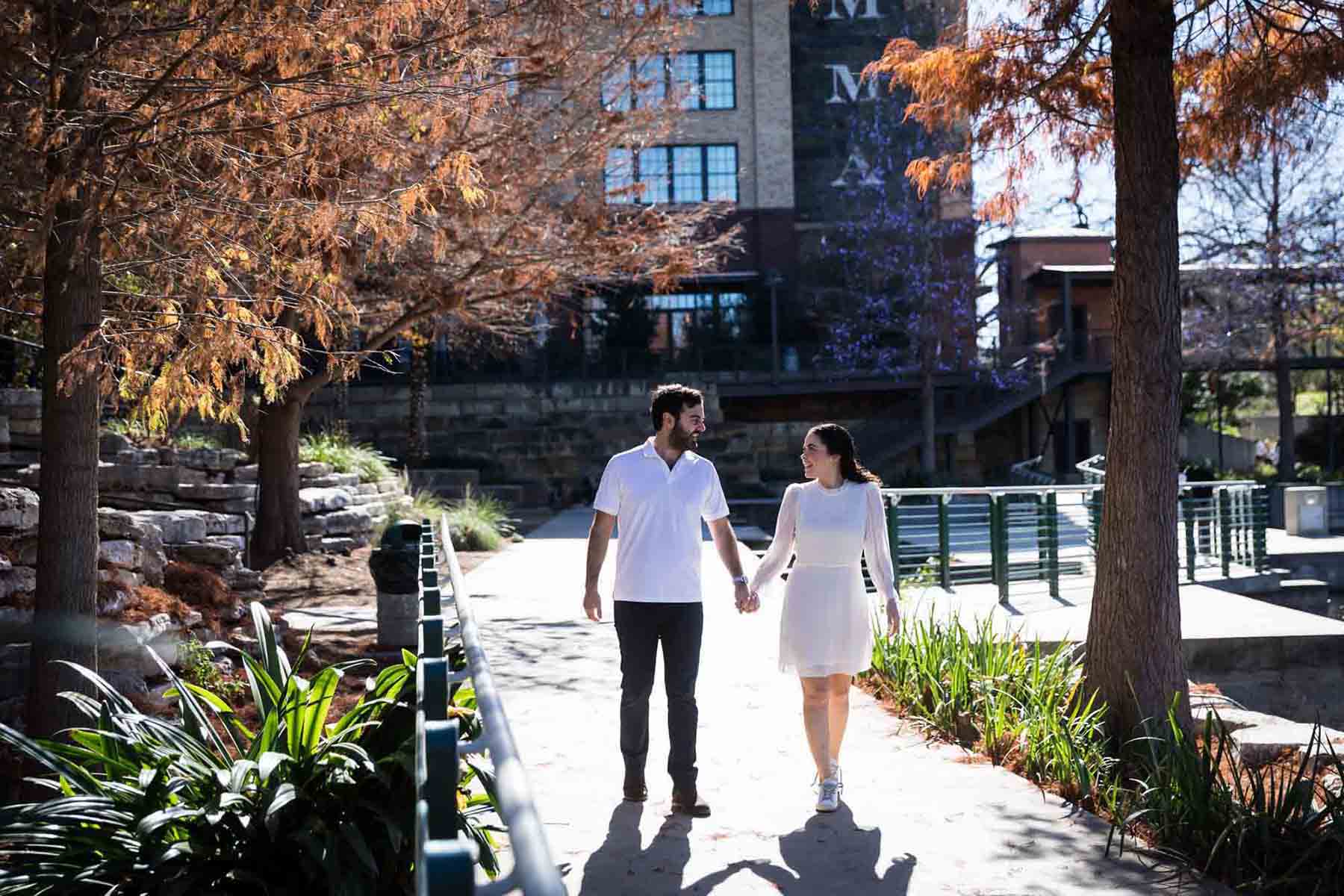 Couple holding hands and walking along the Riverwalk during a Pearl engagement portrait session