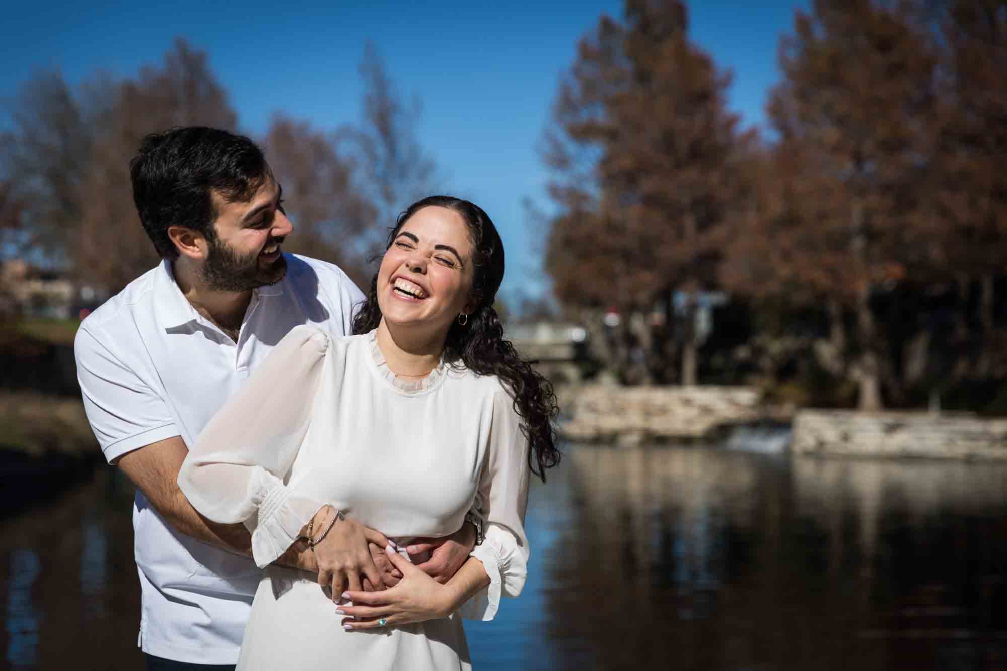 Couple laughing with man hugging woman from behind in front of river during a Pearl engagement portrait session