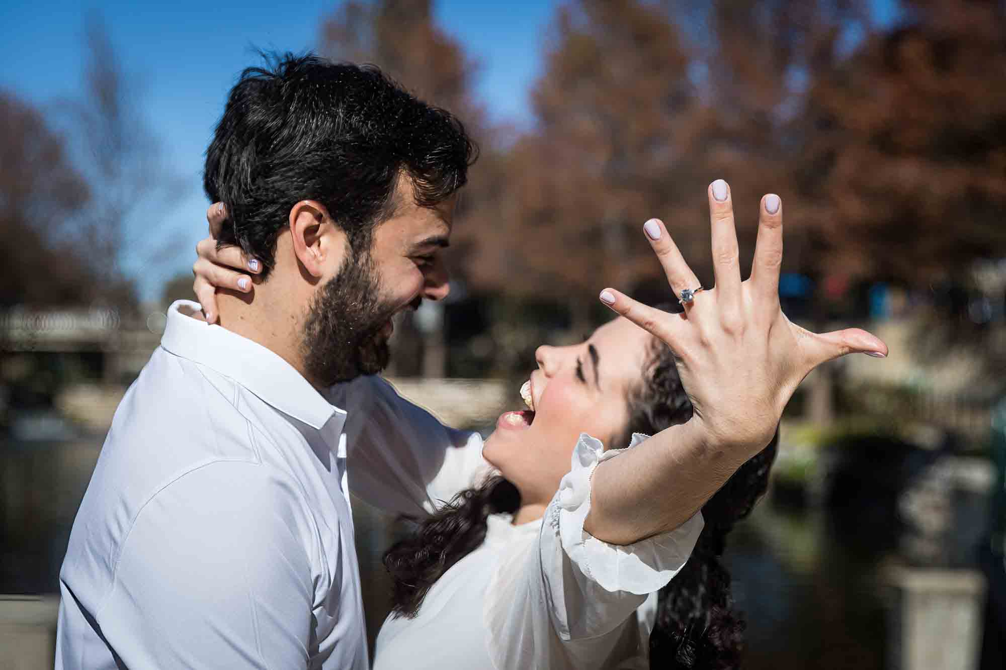 Couple laughing with woman holding hand out showing engagement ring during a Pearl engagement portrait session