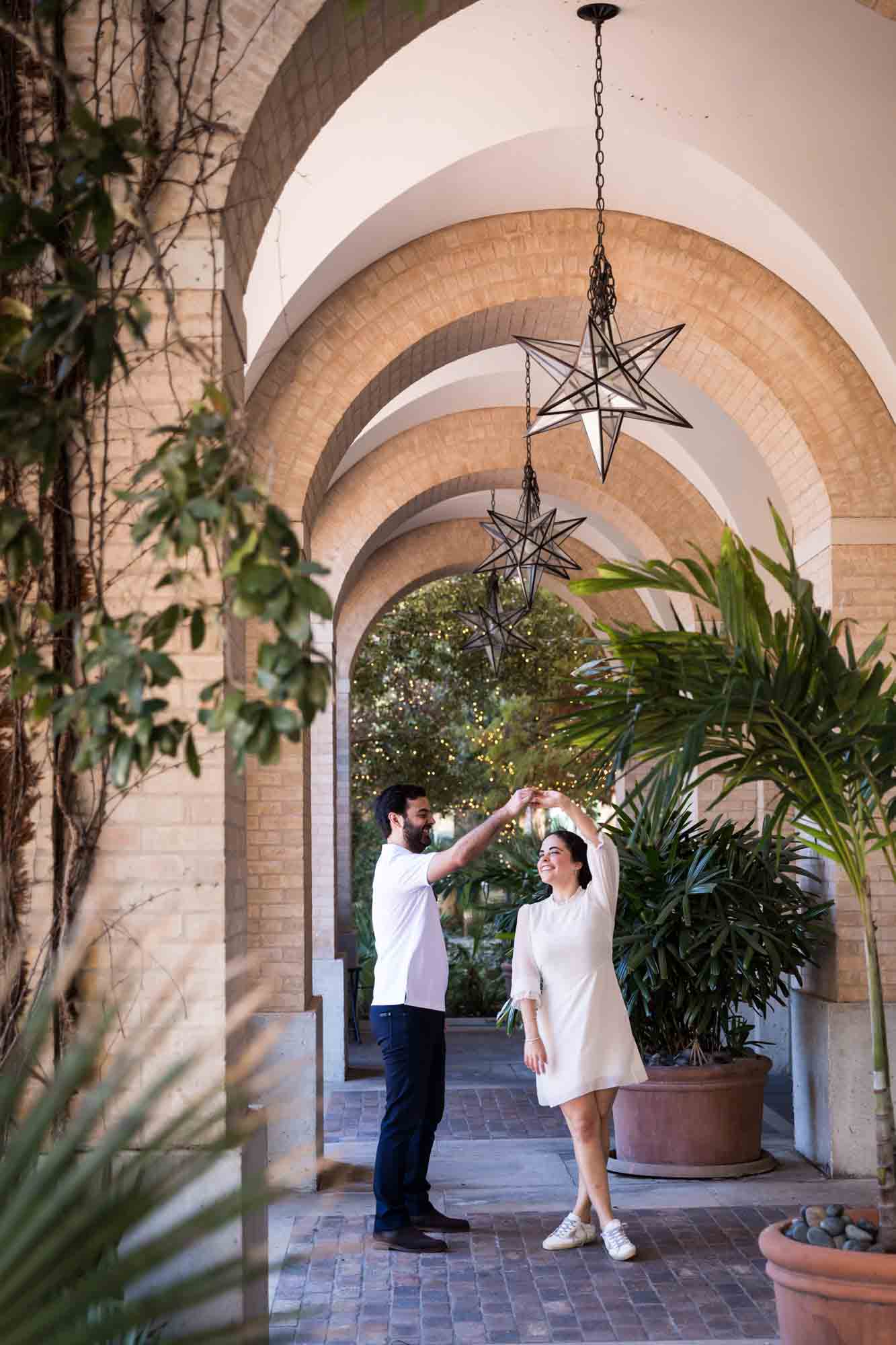 Couple dancing under brick archway with star-shaped lights during a Pearl engagement portrait session