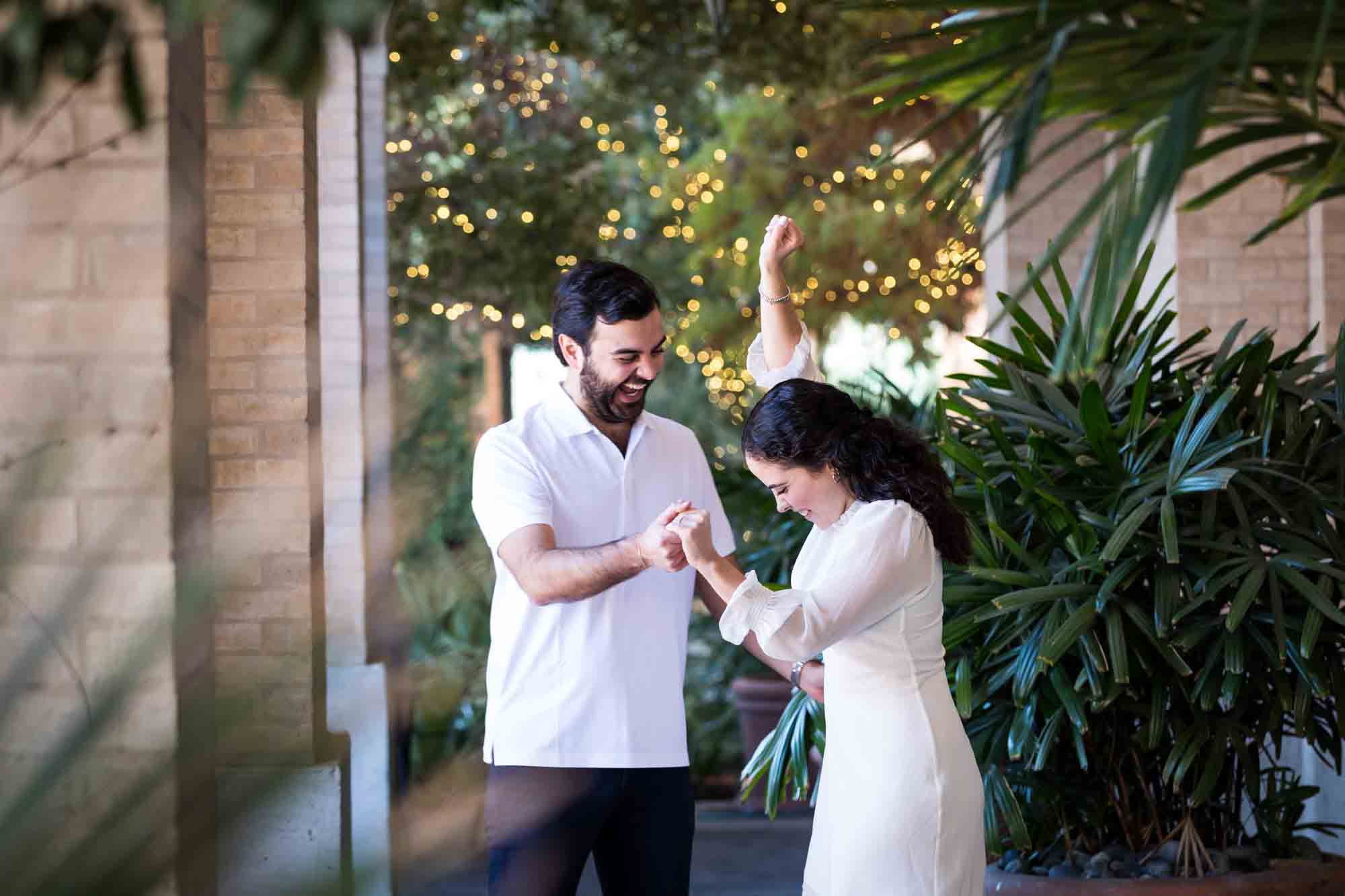 Couple dancing in front of palm trees on patio during a Pearl engagement portrait session