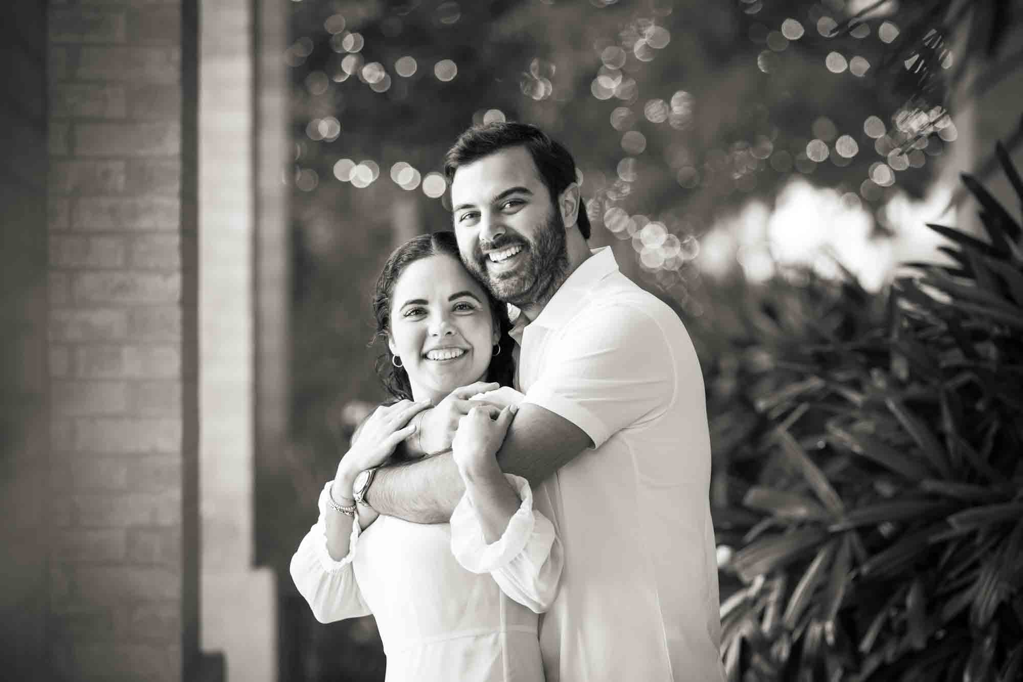 Black and white photo of man hugging woman from behind during a Pearl engagement portrait session