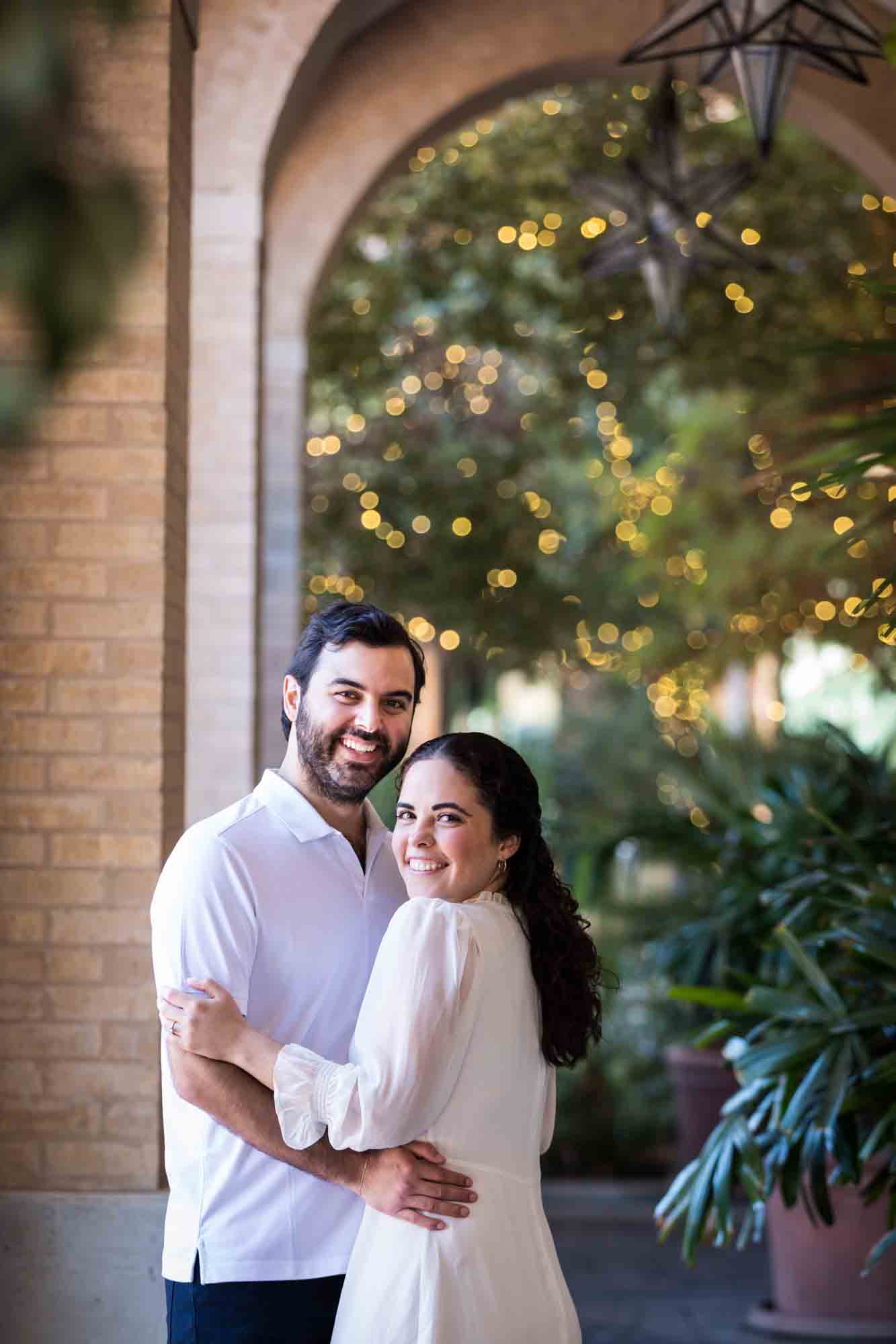 Couple hugging in brick patio by palm trees during a Pearl engagement portrait session
