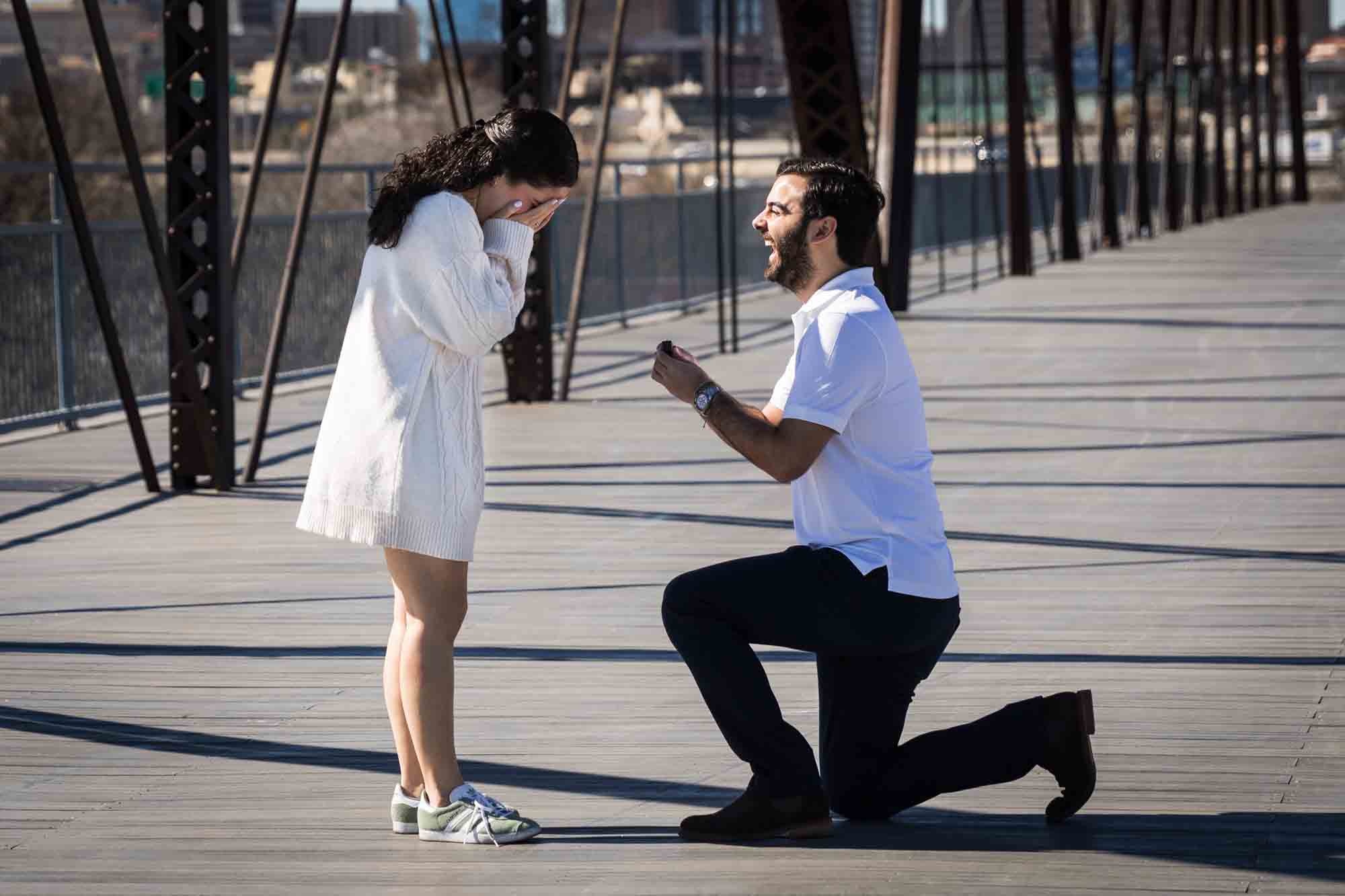 Man on one knee in front of woman for a Hays Street Bridge proposal