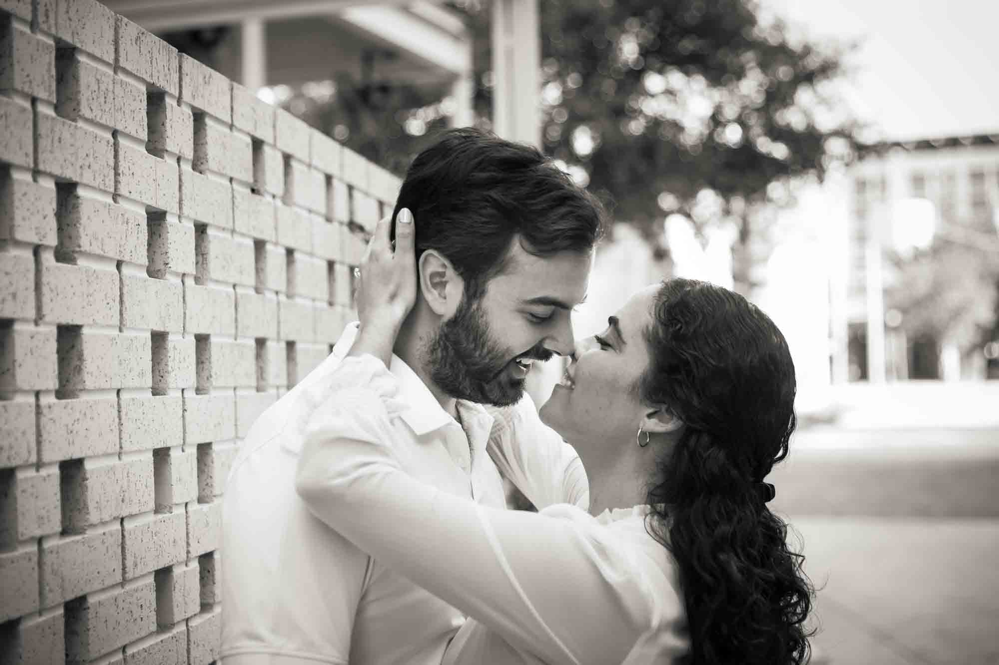 Black and white photo of woman hugging man in front of stone fence during a Pearl engagement portrait session