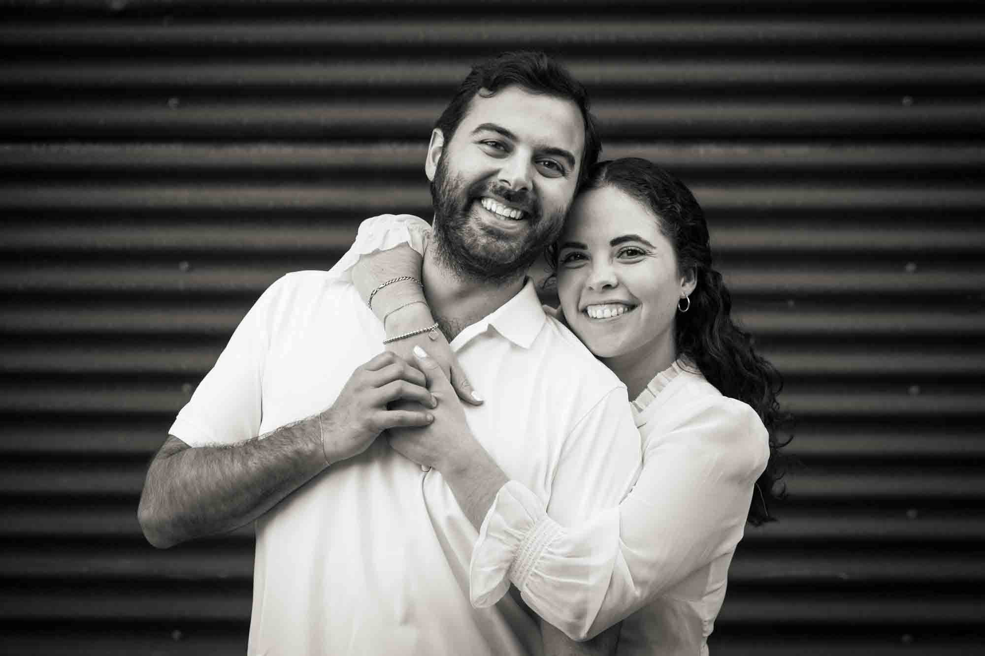 Black and white photo of couple hugging in front of rusty metal door during a Pearl engagement portrait session