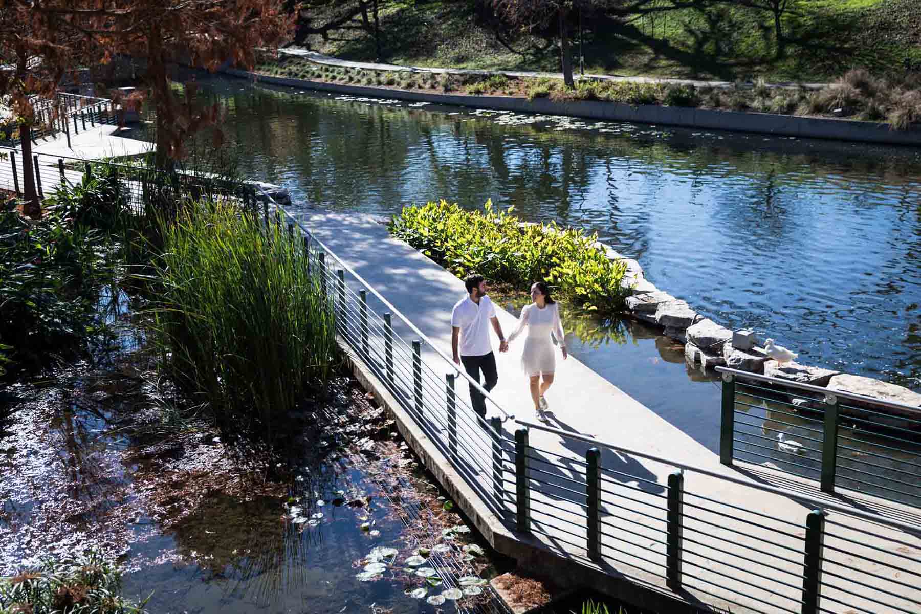 Couple walking hand-in-hand on pathway in front of Riverwalk during a Pearl engagement portrait session