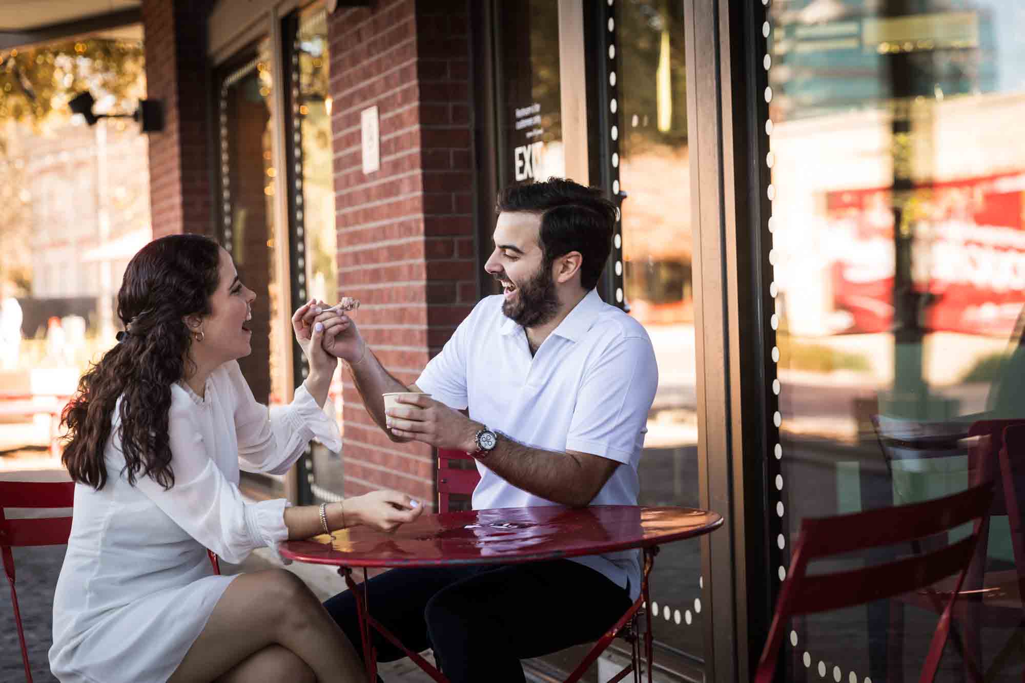 Man feeding woman ice cream while sitting at red table during a Pearl engagement portrait session
