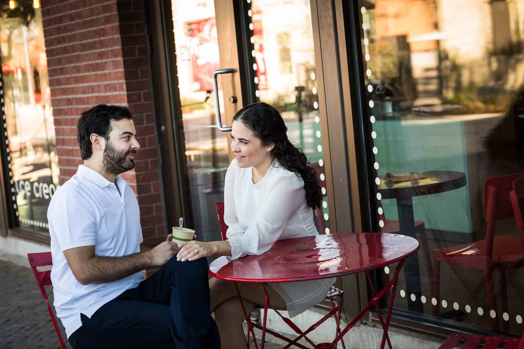 Couple looking at each other while sitting at red table during a Pearl engagement portrait session