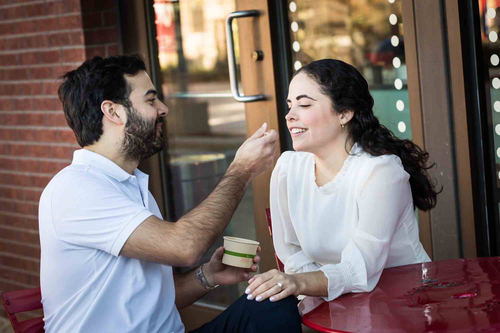 Man feeding woman ice cream at red table during a Pearl engagement portrait session