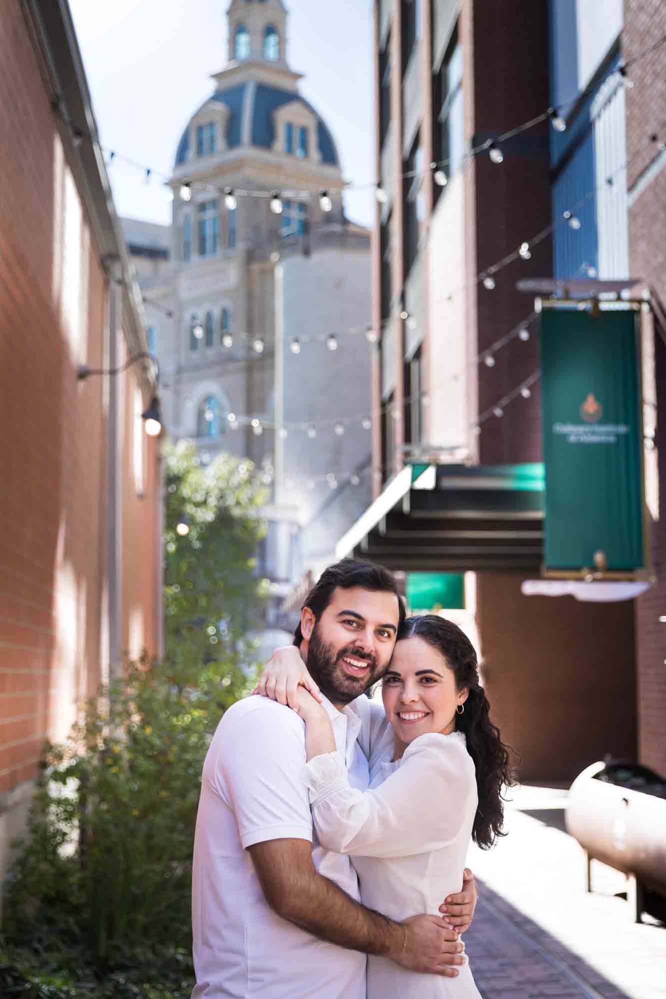 Couple hugging in alleyway with string lights and Pearl Brewery Building in background during a Pearl engagement portrait session