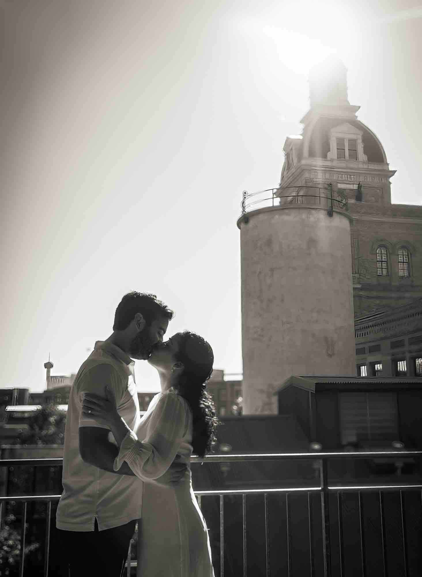 Black and white photo of couple kissing in front of Pearl Brewery Building during a Pearl engagement portrait session