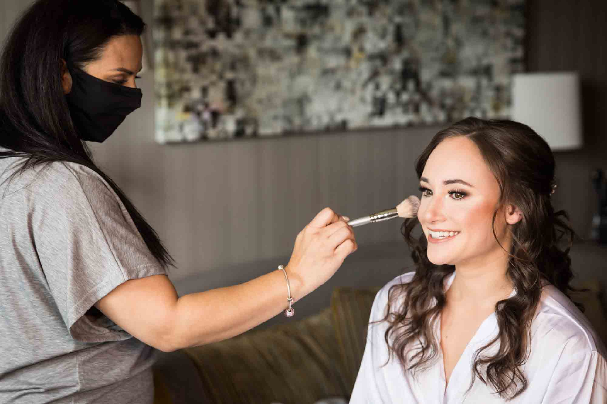 Woman in white robe having blush applied to her cheek for an article on how to find a San Antonio wedding photographer