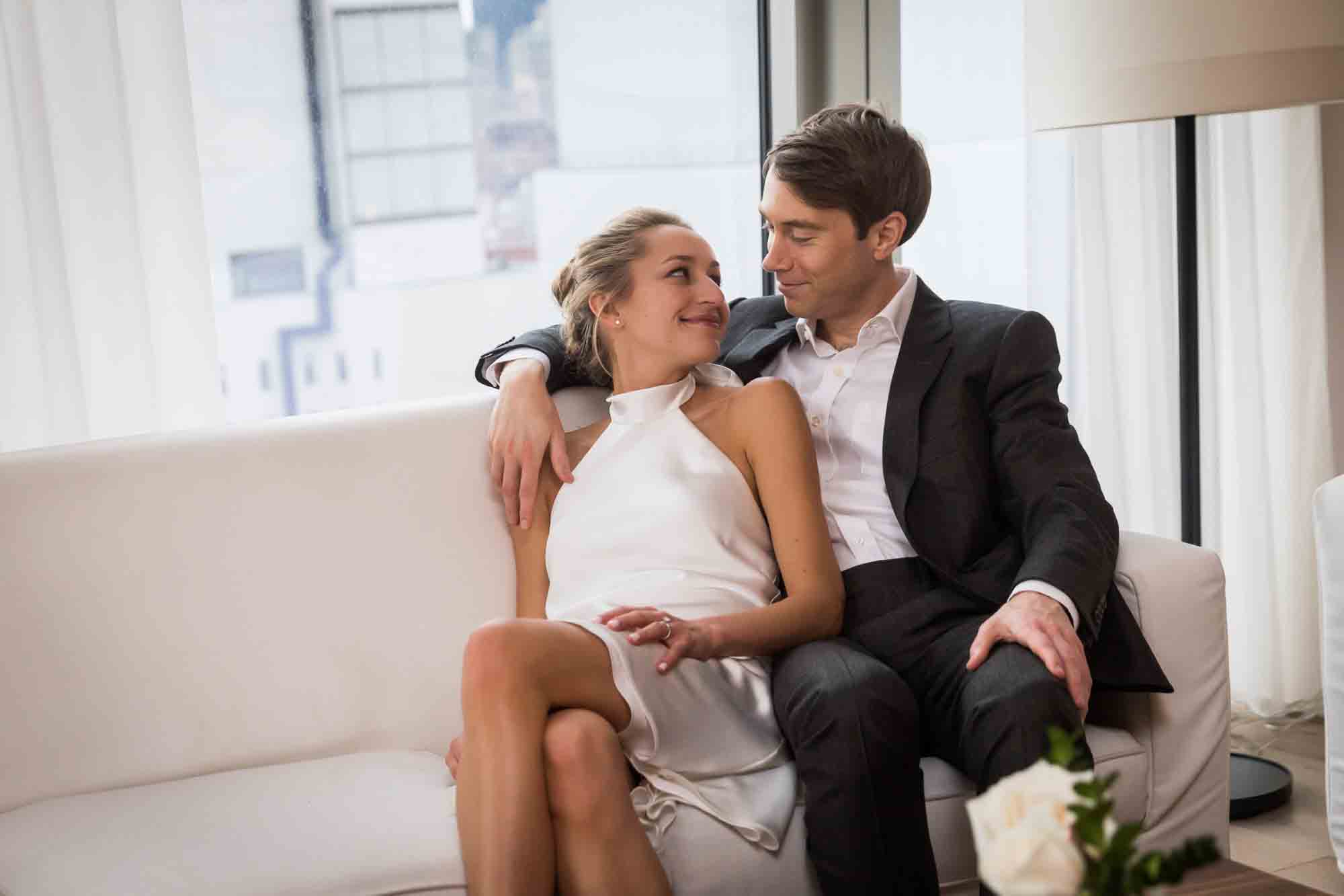 Bride and groom sitting close on white couch in hotel room