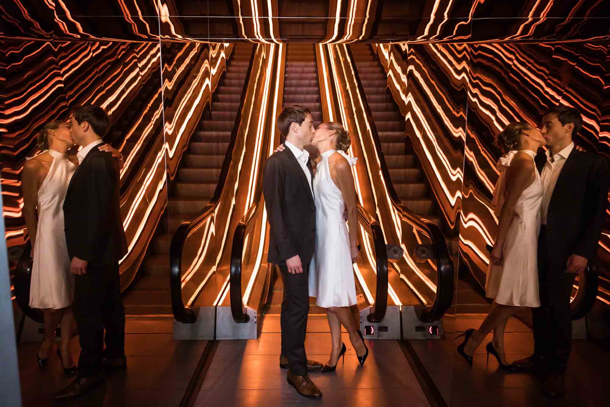 Bride and groom kissing in front of escalators with neon yellow lights