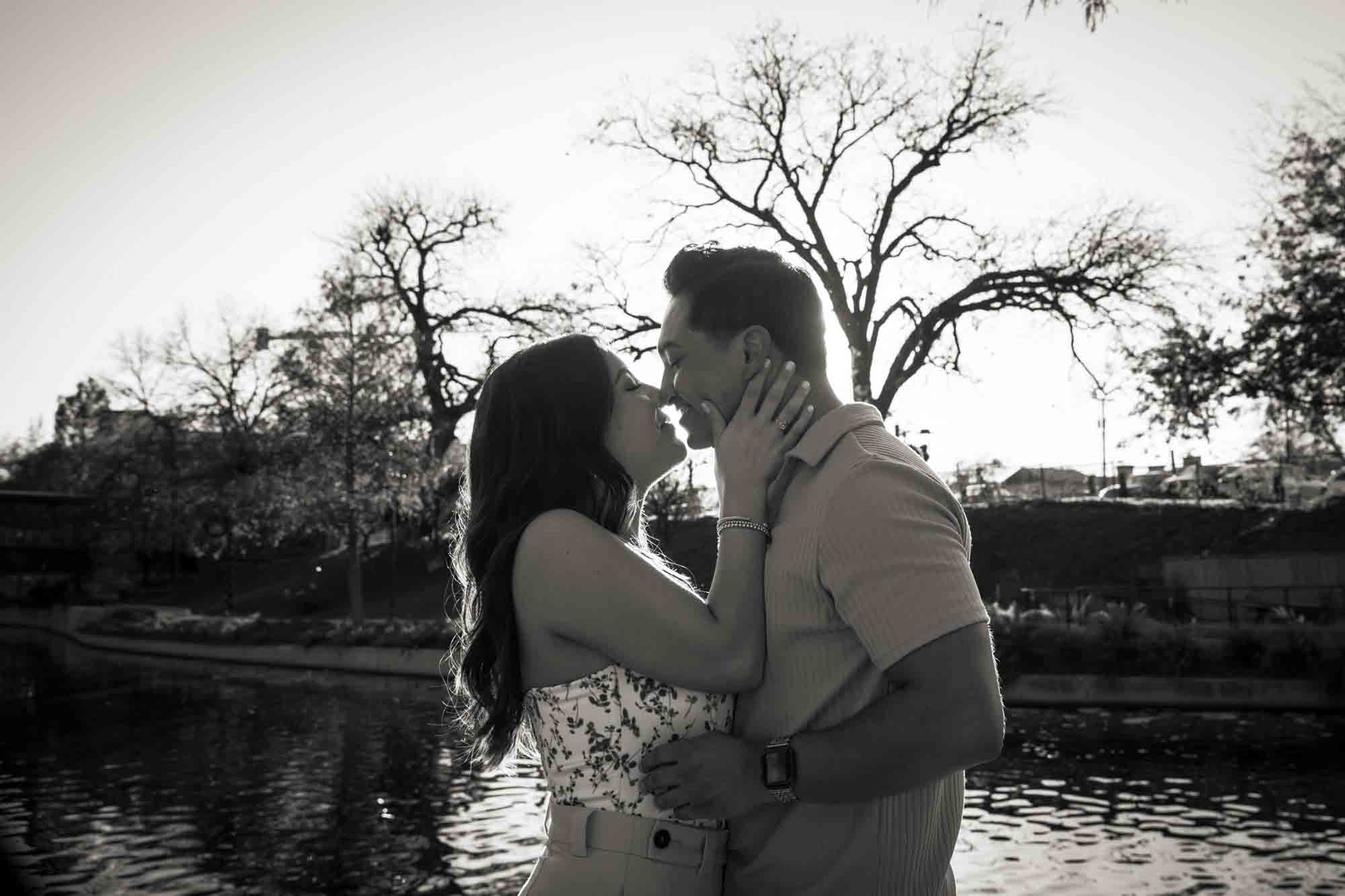 Black and white photo of couple kissing with Riverwalk in the background
